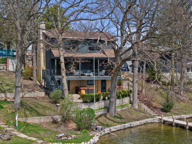 rear view of property with stairway, a deck with water view, board and batten siding, a jacuzzi, and roof with shingles