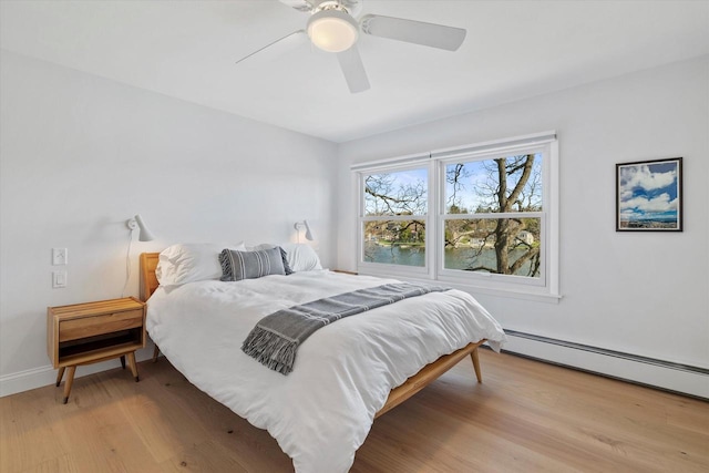 bedroom with a baseboard heating unit, ceiling fan, baseboards, and light wood-type flooring