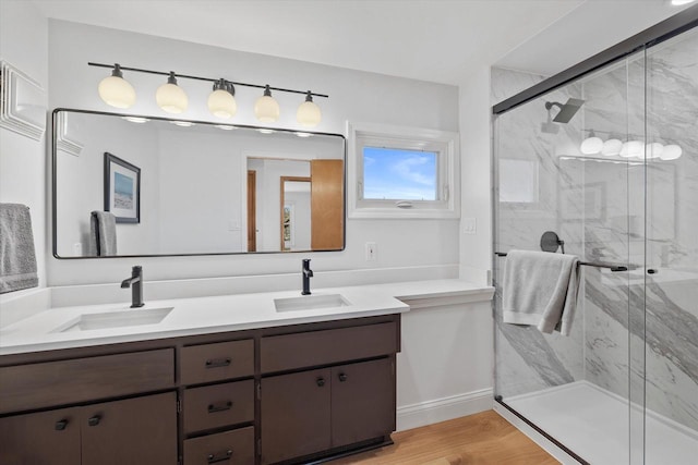 full bathroom featuring a marble finish shower, double vanity, a sink, and wood finished floors