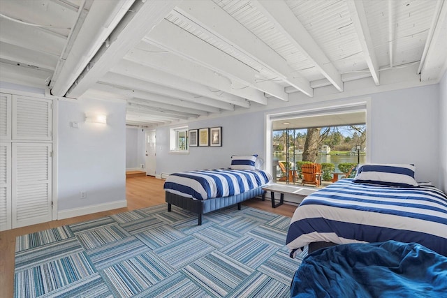 bedroom featuring beamed ceiling, a water view, access to outside, baseboards, and wood finished floors