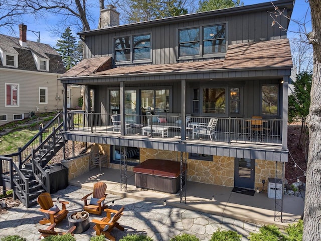 back of house featuring board and batten siding, a patio, a jacuzzi, stone siding, and an outdoor fire pit