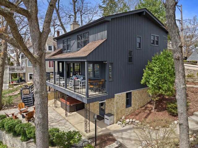 back of property with a patio, a wooden deck, a chimney, stone siding, and roof with shingles