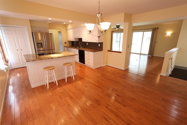 kitchen featuring decorative backsplash, a kitchen island, light wood finished floors, black dishwasher, and stainless steel fridge
