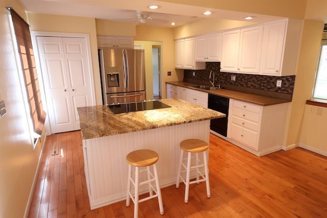 kitchen with decorative backsplash, a kitchen island, black appliances, light wood finished floors, and white cabinetry