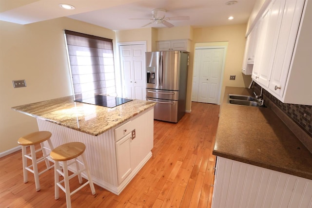 kitchen featuring black electric cooktop, a sink, stainless steel refrigerator with ice dispenser, a ceiling fan, and a kitchen breakfast bar