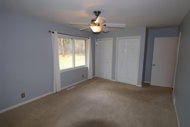 unfurnished bedroom featuring carpet flooring, visible vents, multiple closets, and baseboards