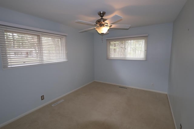 carpeted spare room featuring baseboards, visible vents, and ceiling fan