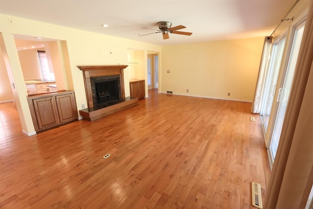 unfurnished living room with a high end fireplace, light wood finished floors, ceiling fan, and visible vents