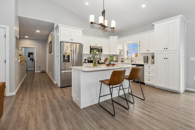 kitchen featuring white cabinets, appliances with stainless steel finishes, a kitchen island, light countertops, and wood finished floors