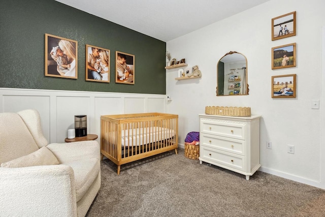 bedroom with wainscoting, a decorative wall, a nursery area, and carpet floors