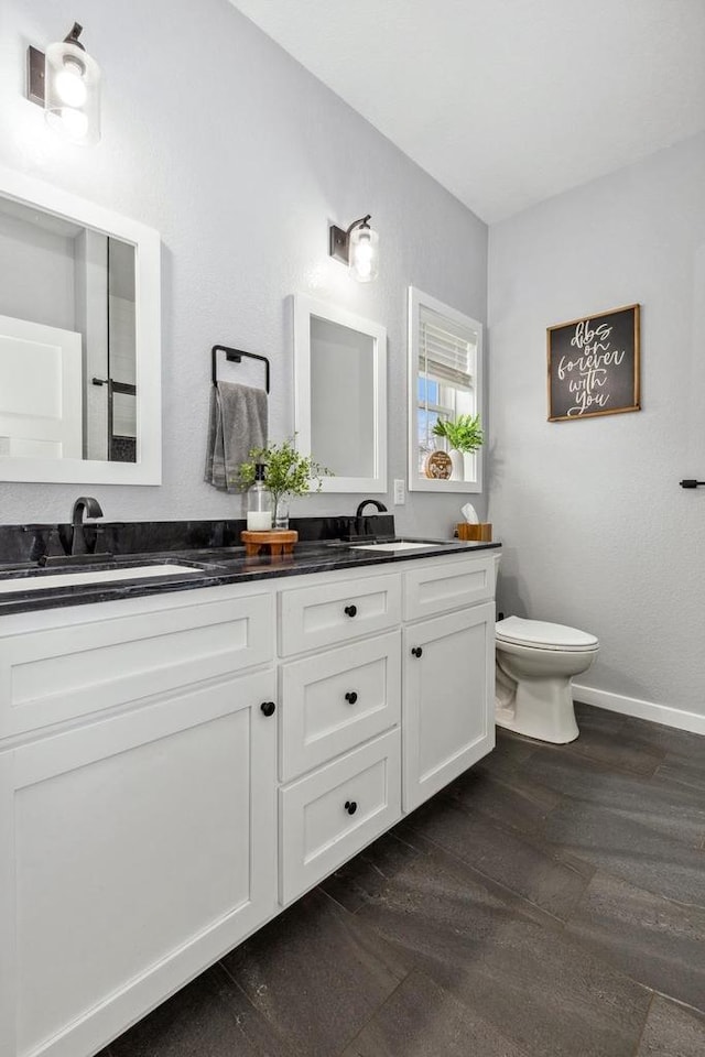 bathroom featuring double vanity, wood finished floors, toilet, and a sink