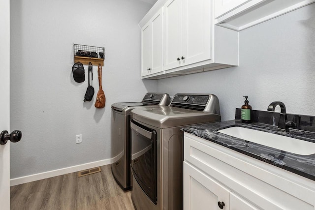 laundry room featuring washer and dryer, light wood-style floors, cabinet space, a sink, and baseboards