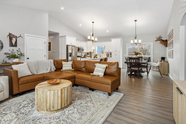 living area with a notable chandelier, high vaulted ceiling, wood finished floors, and a healthy amount of sunlight