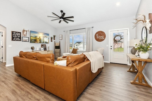 living area with lofted ceiling, ceiling fan, baseboards, arched walkways, and light wood-type flooring