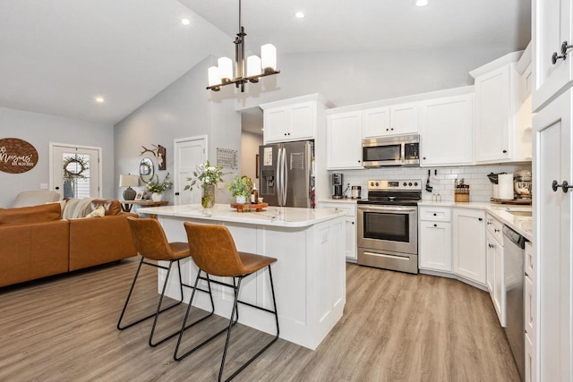 kitchen with white cabinets, appliances with stainless steel finishes, a center island, open floor plan, and high vaulted ceiling