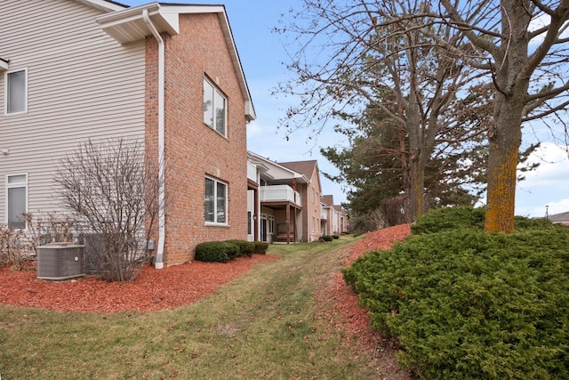 view of property exterior featuring brick siding, central air condition unit, and a lawn