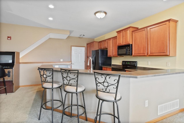 kitchen featuring black appliances, a kitchen bar, visible vents, and light colored carpet