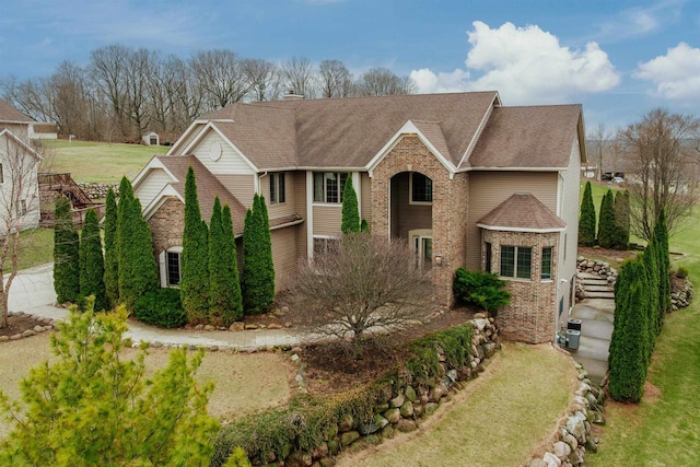 traditional home featuring brick siding, a front yard, and roof with shingles