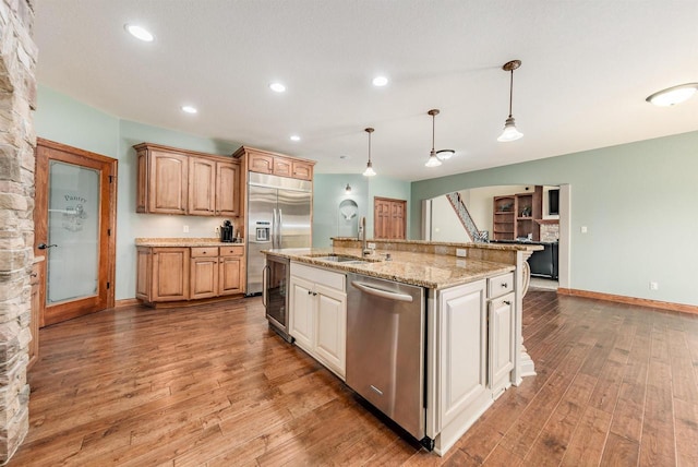 kitchen with a sink, appliances with stainless steel finishes, beverage cooler, light wood-style floors, and hanging light fixtures