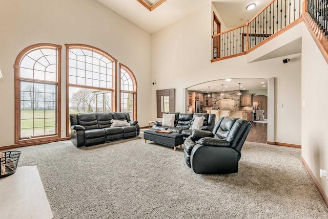 carpeted living area with a towering ceiling, arched walkways, baseboards, and a healthy amount of sunlight