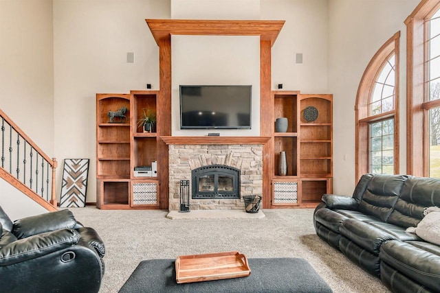 carpeted living room featuring a high ceiling, a stone fireplace, and stairway