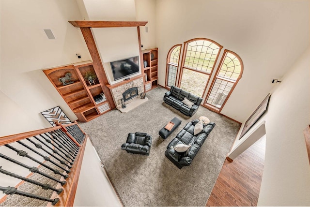 living area featuring a high ceiling, stairway, a fireplace with raised hearth, baseboards, and wood finished floors