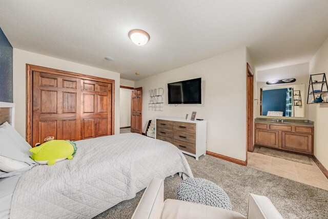 bedroom with ensuite bath, light colored carpet, and baseboards