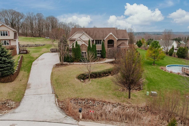 view of front of house with a chimney, brick siding, a front yard, and driveway