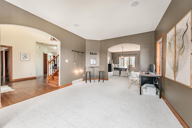 office space featuring baseboards, visible vents, arched walkways, and wood finished floors