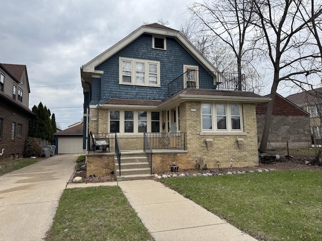 view of front of property with covered porch, brick siding, a front yard, and a detached garage