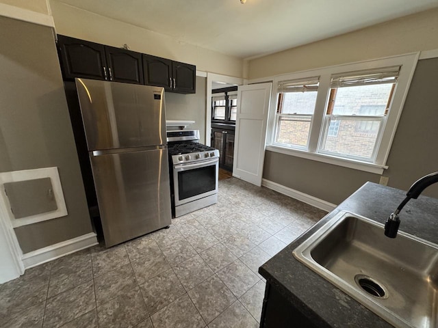 kitchen featuring baseboards, dark countertops, appliances with stainless steel finishes, and a sink