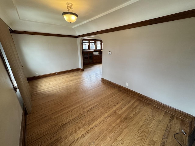 empty room with baseboards, arched walkways, and wood finished floors