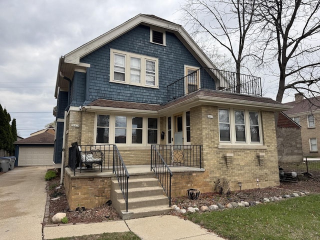 view of front of home with covered porch, brick siding, an outbuilding, a garage, and a balcony