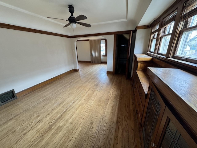 unfurnished living room with a ceiling fan, visible vents, baseboards, arched walkways, and wood finished floors