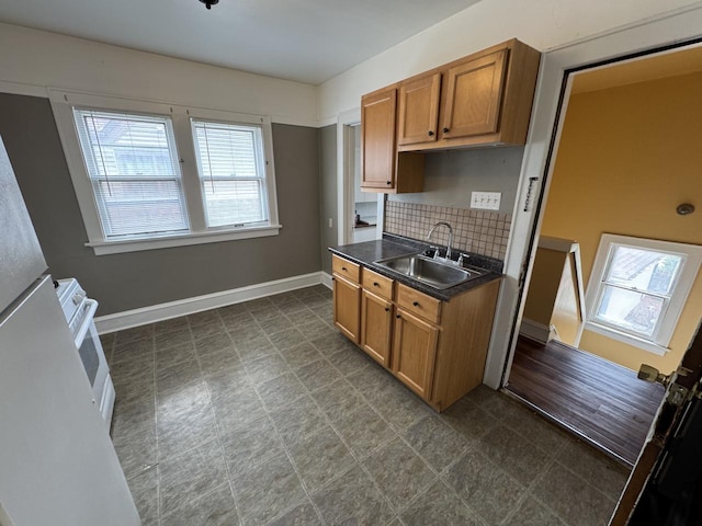 kitchen featuring tasteful backsplash, brown cabinets, range, a sink, and dark countertops