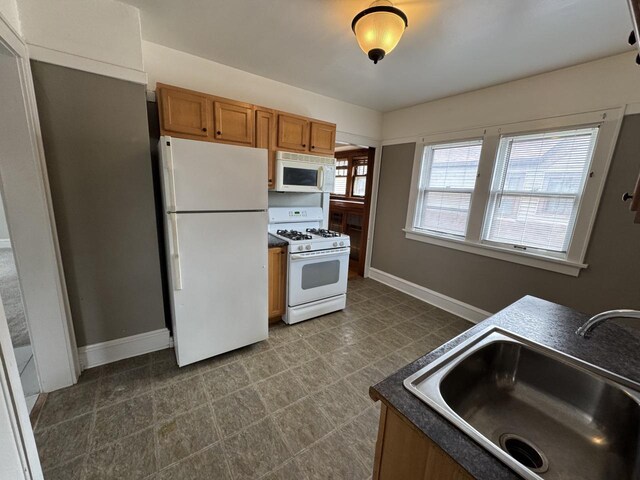 kitchen featuring brown cabinets, a sink, dark countertops, baseboards, and white appliances