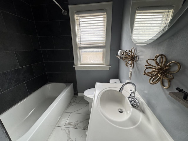 full bathroom featuring washtub / shower combination, toilet, marble finish floor, and baseboards