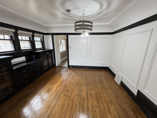 unfurnished dining area featuring crown molding, visible vents, dark wood-style floors, a decorative wall, and a notable chandelier