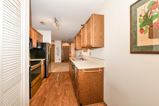 kitchen with brown cabinets, a sink, light wood-style floors, stainless steel appliances, and light countertops
