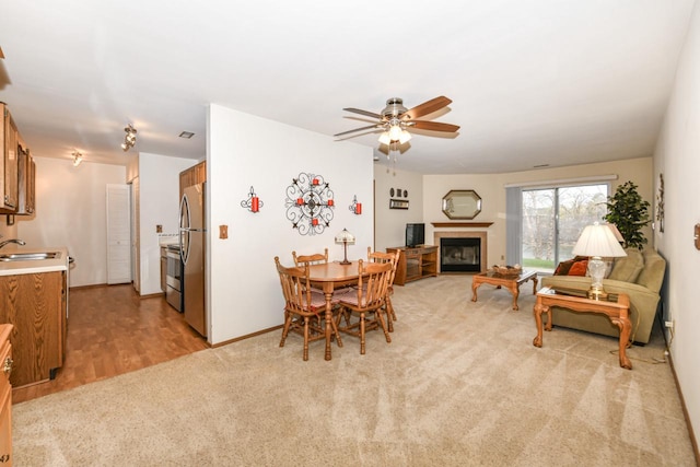 dining room with baseboards, a ceiling fan, light colored carpet, and a glass covered fireplace