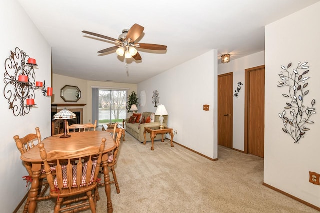 dining space with a ceiling fan, light colored carpet, and baseboards