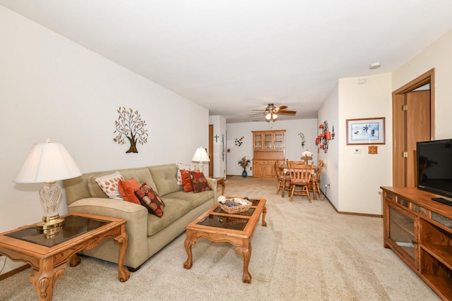 living room featuring baseboards, light carpet, and ceiling fan