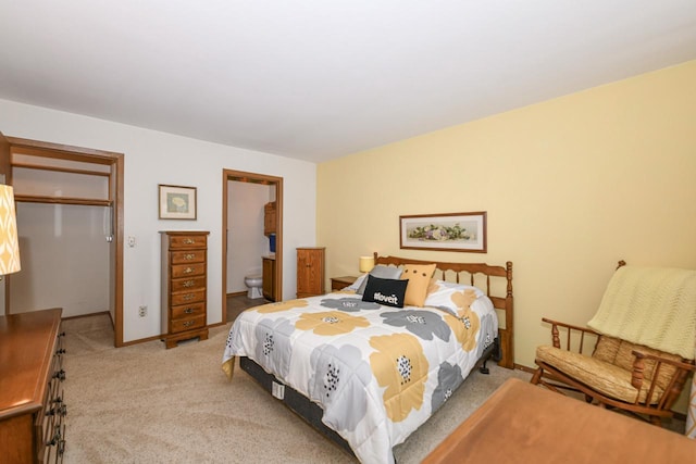 bedroom with a closet, baseboards, light carpet, ensuite bath, and a walk in closet