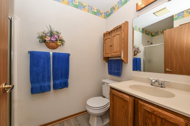 bathroom with wood finished floors, a shower stall, toilet, vanity, and baseboards