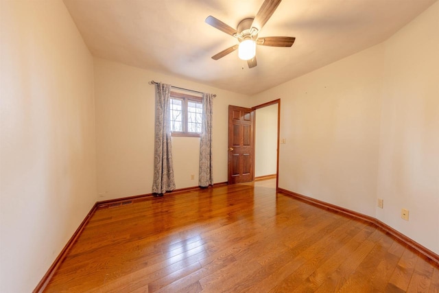 empty room with baseboards, visible vents, wood finished floors, and a ceiling fan