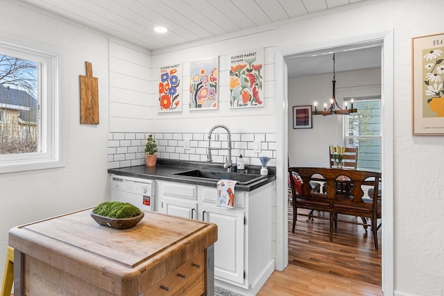 kitchen featuring white dishwasher, dark countertops, an inviting chandelier, a sink, and light wood finished floors