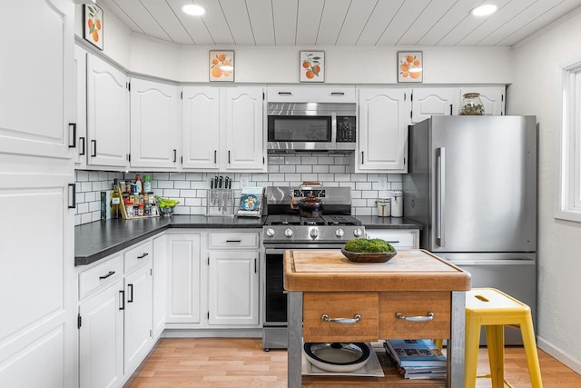 kitchen with dark countertops, stainless steel appliances, light wood-style flooring, and white cabinetry