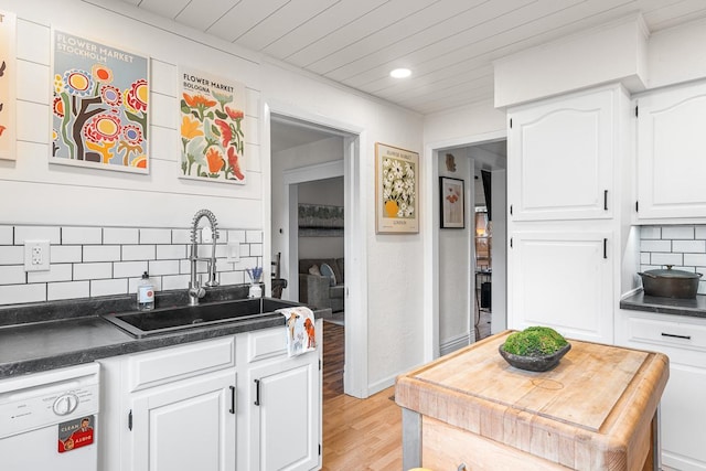 kitchen with white dishwasher, dark countertops, backsplash, and a sink