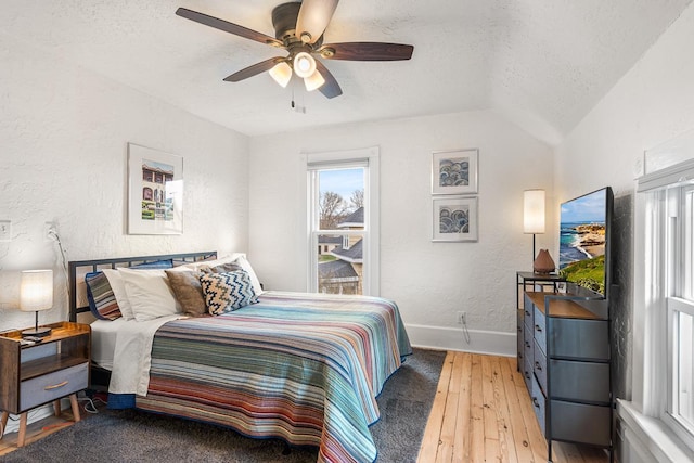 bedroom featuring a textured wall, lofted ceiling, baseboards, a textured ceiling, and light wood-style flooring