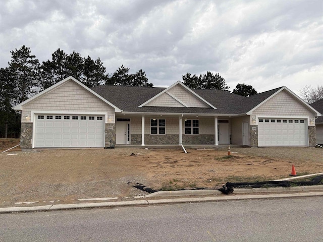 view of front of property with covered porch, driveway, an attached garage, and stone siding